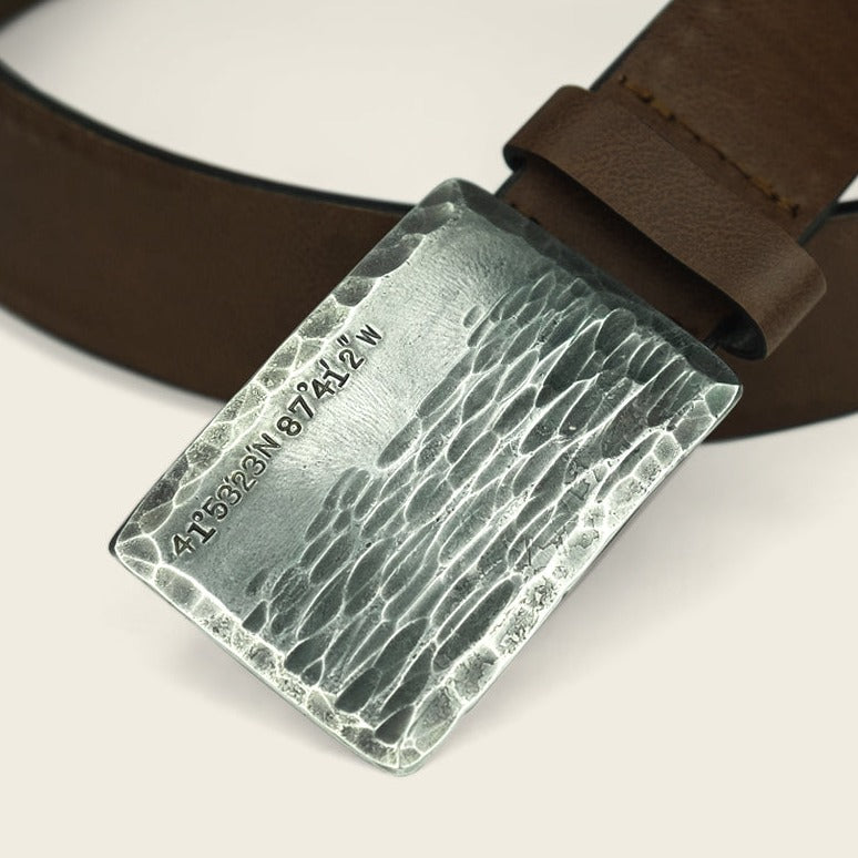 A close-up of a brown leather belt from Cityboy Forge, featuring a custom coordinates buckle—a rectangular, textured silver design engraved with 41°5328N 87°4432W.