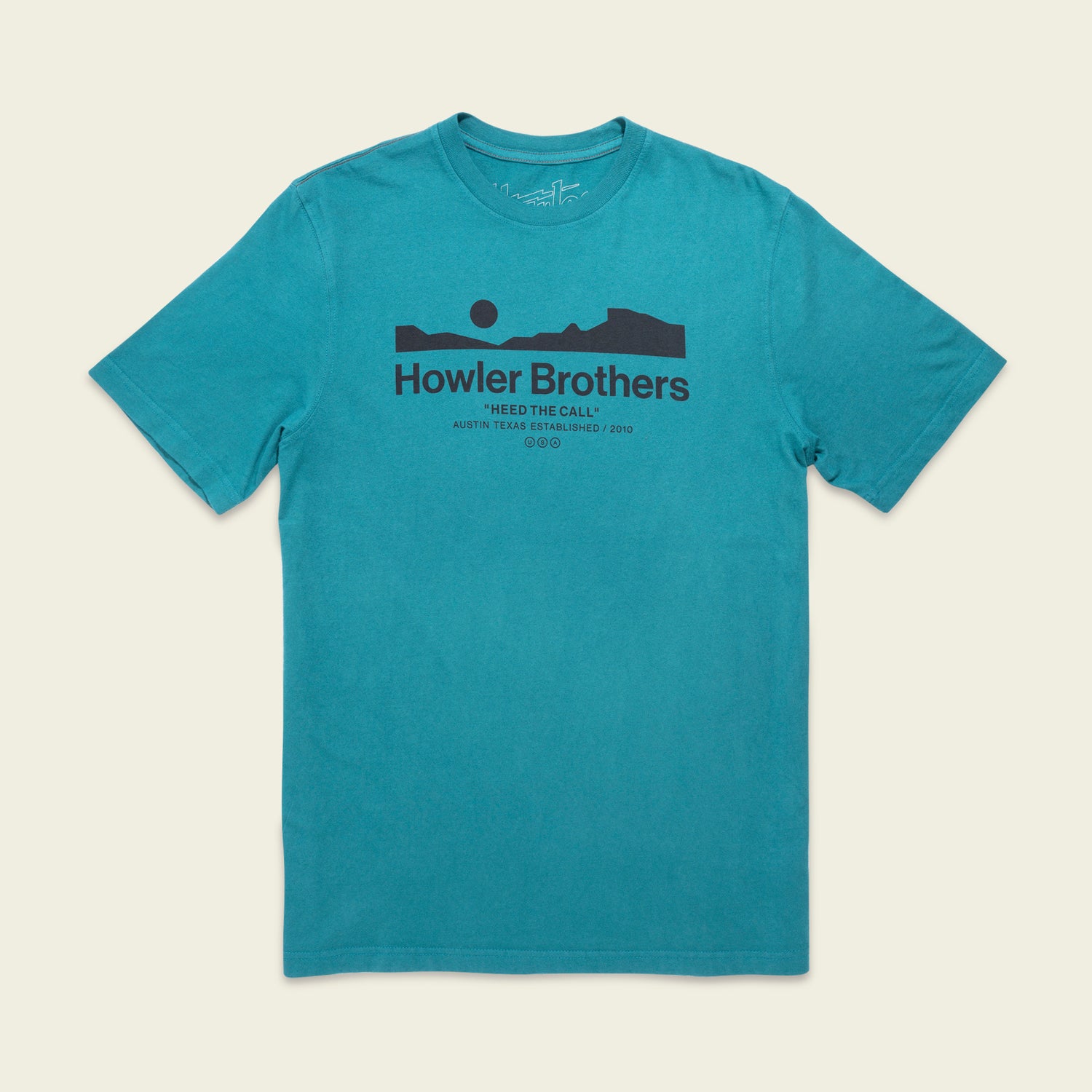 A teal short-sleeve T-shirt featuring experimental artwork: a black graphic of a mountain landscape and sun. The text reads Howler Brothers and Heed The Call, Austin, Texas, Established 2010 beneath the graphic.
