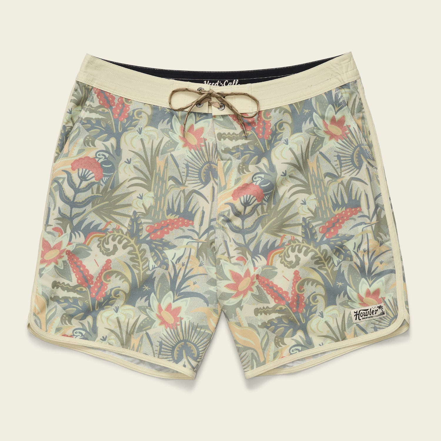 Beige Bruja Boardshorts with a tropical botanical pattern in green, red, and orange shades, crafted from stretchy fabric and featuring an adjustable drawstring waistband, draining front pockets, and a small Howler logo patch near the hem.
