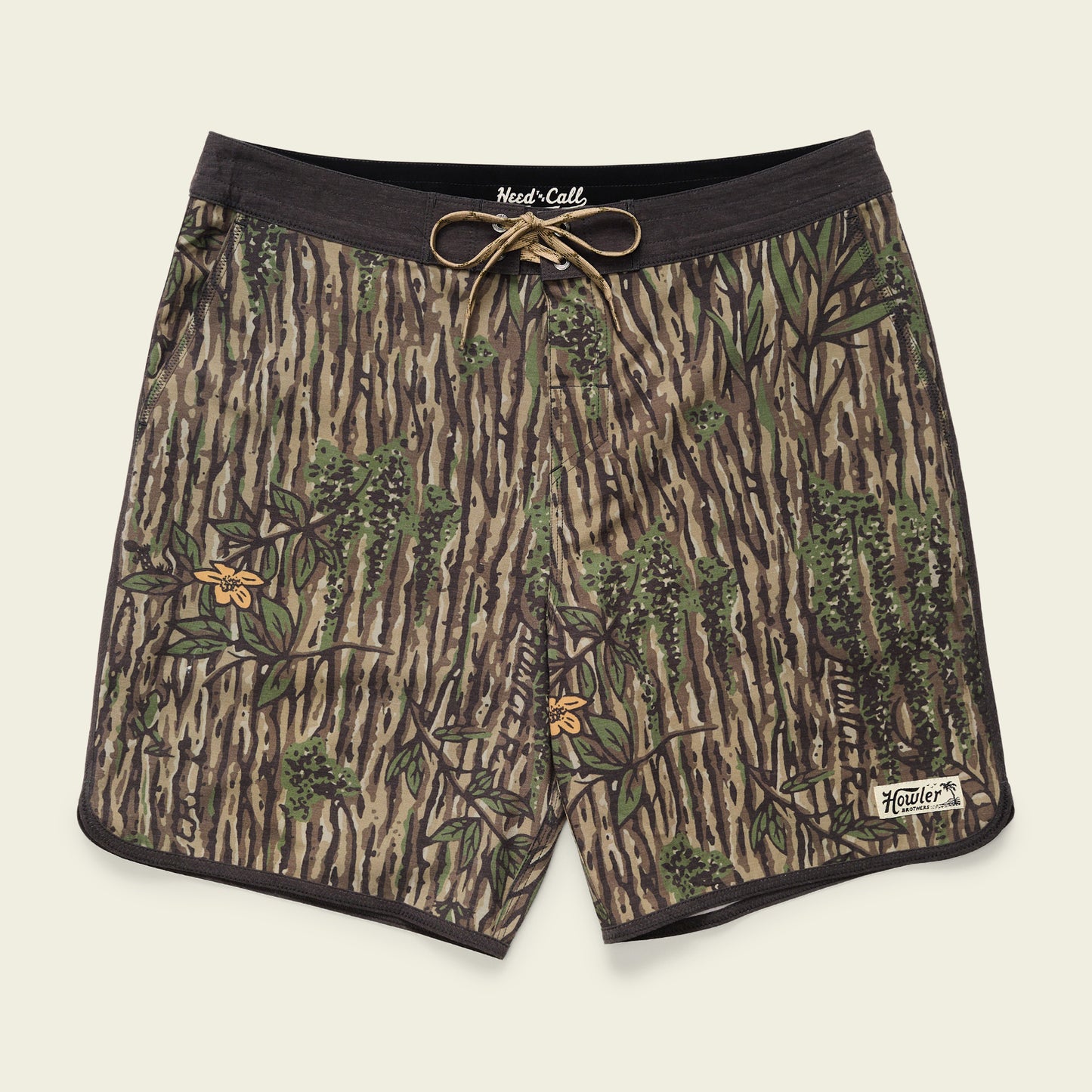 A pair of Bruja Boardshorts with a tree bark and leaves camouflage pattern, featuring stretchy fabric, a black waistband, brown drawstring, draining front pockets, and a small white Howler label near the bottom hem. - View 1