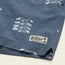 Close-up of blue swim trunks featuring white seagull patterns, an elastic waistband, and a stitched Howler Brothers label on the hem with a palm tree graphic.