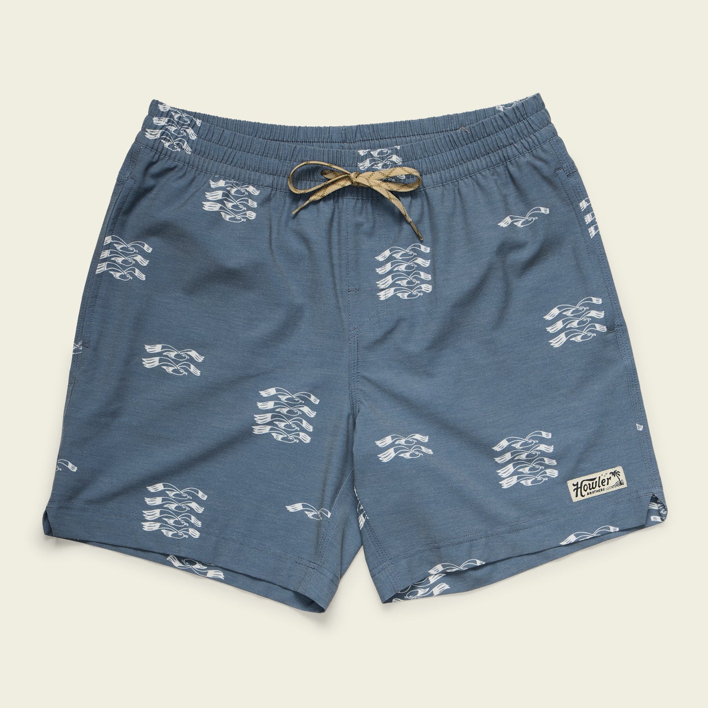 Blue boardshorts with a white abstract pattern, an elastic waistband with a beige drawstring, and a small Howler patch on the lower left leg, displayed flat on a light background. - View 1