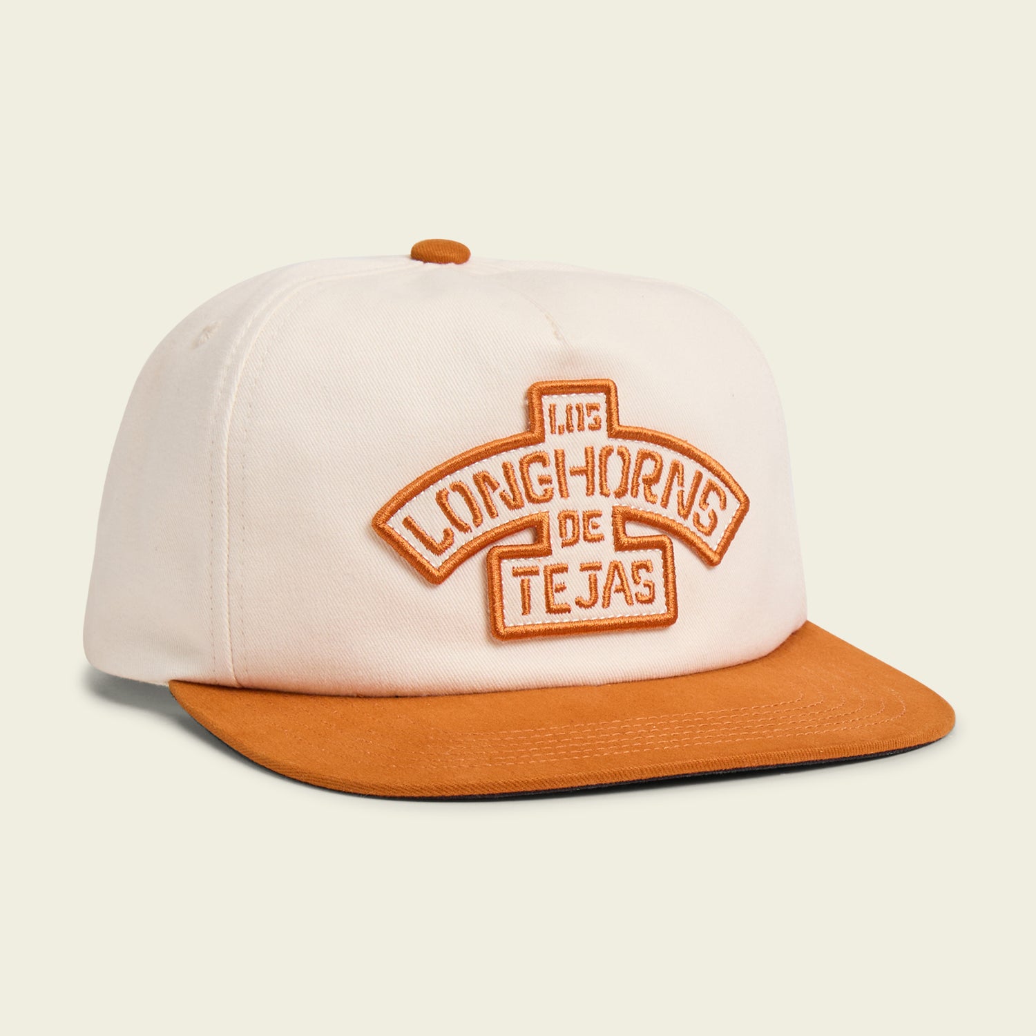 This unstructured snapback baseball cap features a white crown with a burnt orange brim and button. The front showcases Los Longhorns de Tejas in orange embroidery, honoring the University of Texas Longhorns and the year 1915.