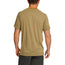 A man stands with his back to the camera, wearing a light brown shortsleeve tech shirt made from a polyester spandex blend and dark gray shorts. Subtle text lines the bottom hem of the shirt. The background is plain white.